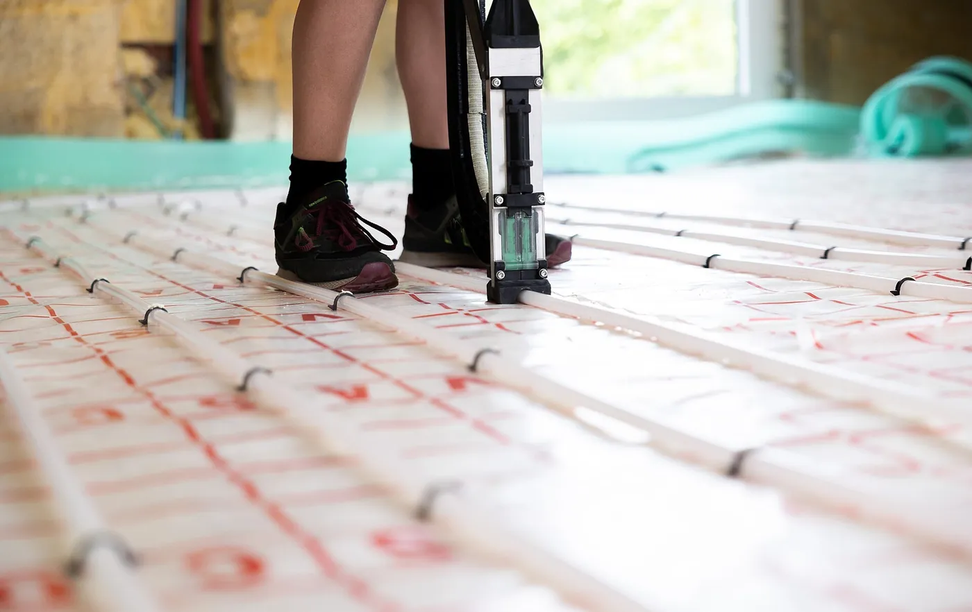 Installateur fixant à l'agrafeuse à tubes les serpentins blancs de plancher chauffant sur un isolant quadrillé de rouge