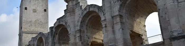 Arcades en pierre de l'amphithéâtre romain d'Arles et l'une de ses tours médiévales, sous un ciel nuageux