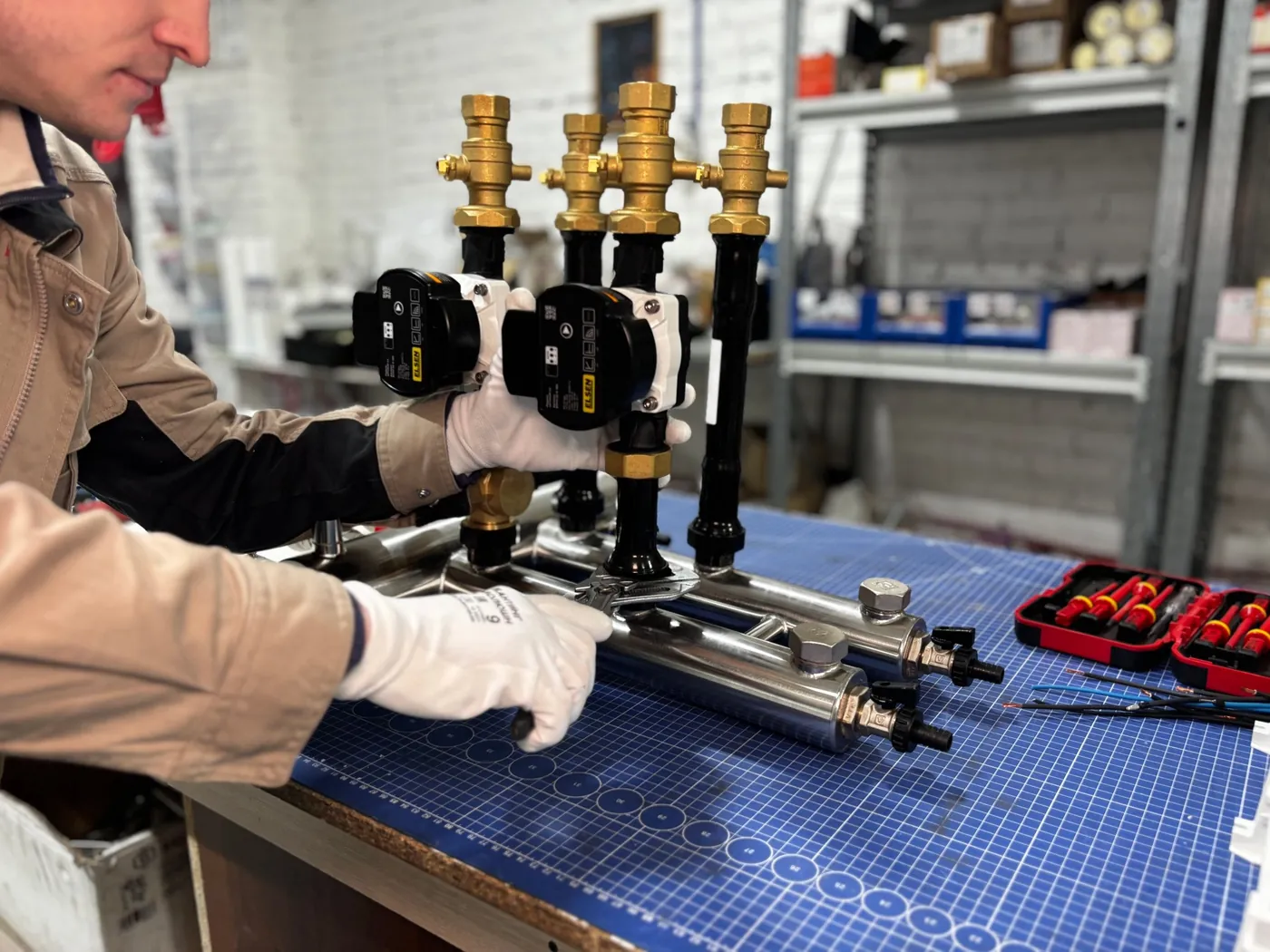 Technicien ganté assemblant des groupes de pompage noirs et laiton sur un collecteur inox, posé sur un tapis de découpe bleu