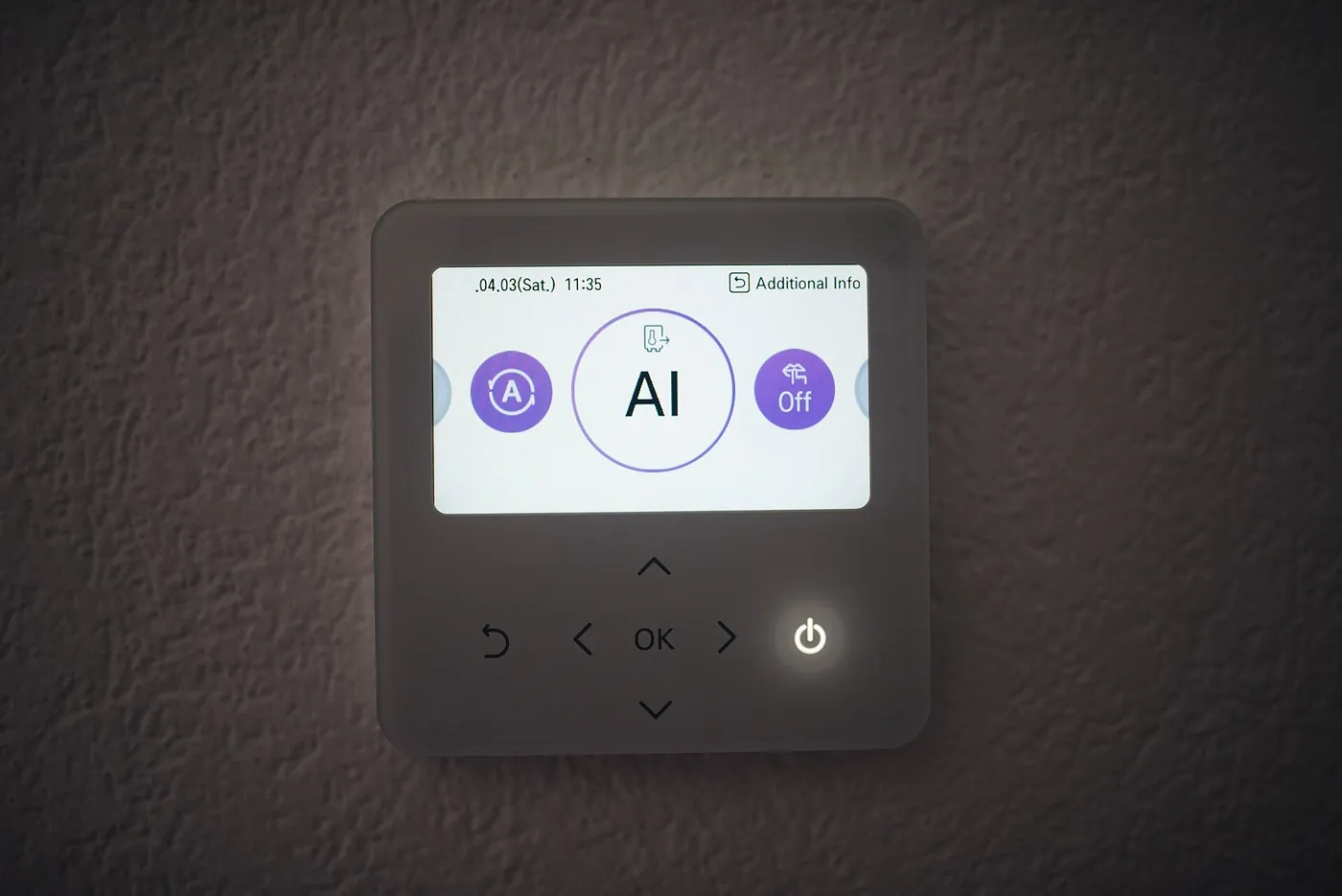 Gros plan d'un écran de commande tactile de pompe à chaleur, cadre noir et touches lumineuses, fixé sur un mur crépi