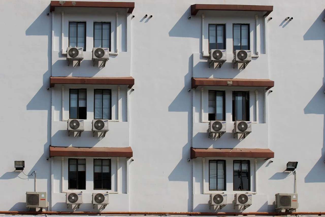 Façade d'immeuble blanche où une unité extérieure de climatisation réversible est fixée sous chaque paire de fenêtres