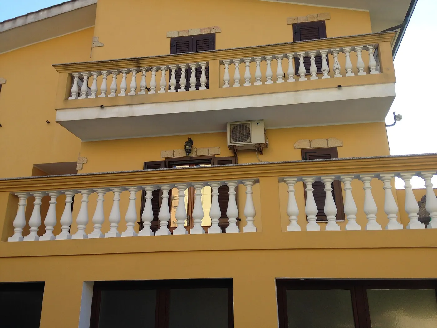 Façade jaune à deux étages de balcons à balustres blancs, unité extérieure fixée sous la dalle du balcon supérieur