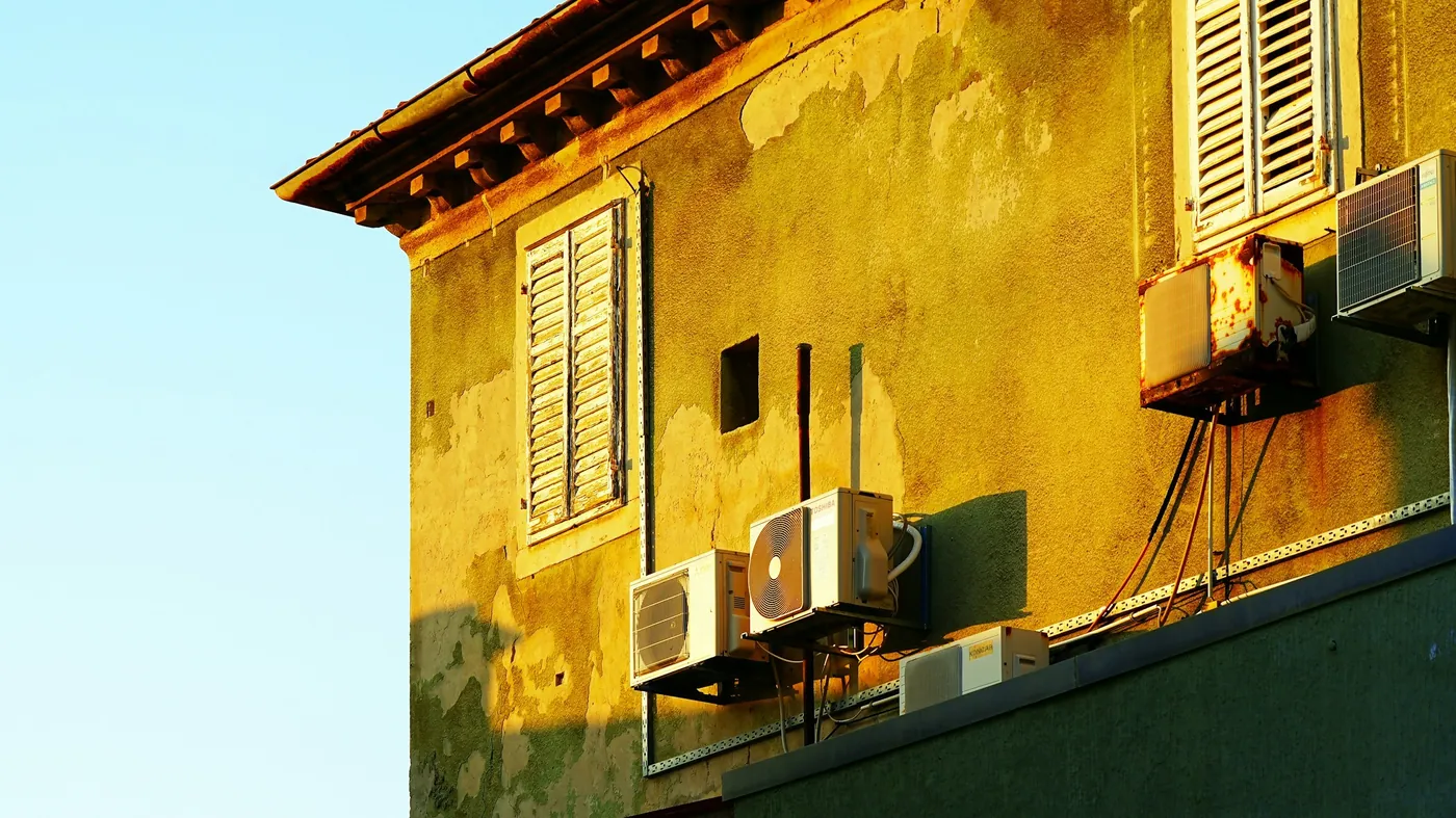 Façade ancienne ocre au crépi écaillé, volets persiennés et quatre unités extérieures sur consoles, comme on en voit à Manosque