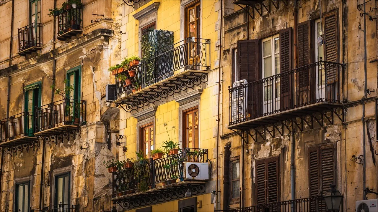 Façades anciennes ocre et jaunes aux balcons en fer forgé fleuris, avec une unité extérieure fixée sous un balcon