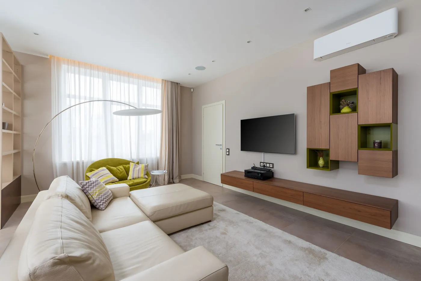 Grand salon beige avec canapé d'angle en cuir crème, fauteuil vert, meubles en noyer suspendus et unité intérieure murale en hauteur