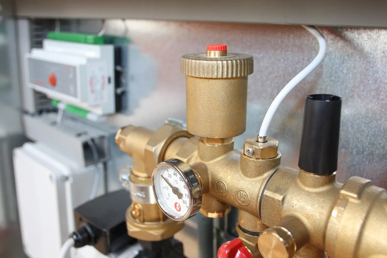 Gros plan d'un groupe hydraulique en laiton avec manomètre gradué, purgeur à capuchon rouge et boîtier de régulation en arrière-plan