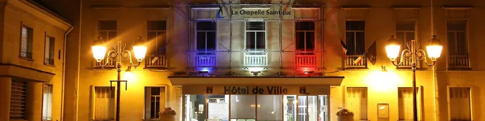 Façade de l'hôtel de ville de La Chapelle-Saint-Luc illuminée de nuit, avec ses lampadaires et ses fenêtres aux couleurs bleu, blanc, rouge