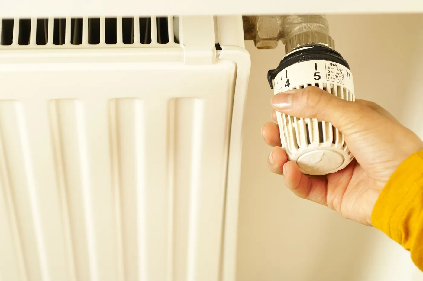 Main qui tourne la tête thermostatique blanche d'un radiateur en acier, réglée entre les positions 4 et 5