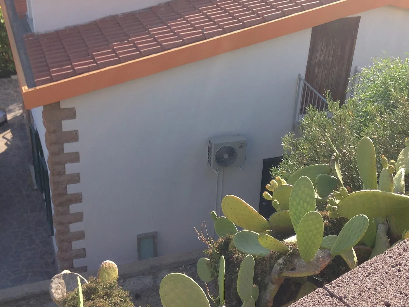 Vue plongeante sur une maison blanche à toit de tuiles et chaînage d'angle en pierre, unité extérieure murale, figuiers de Barbarie