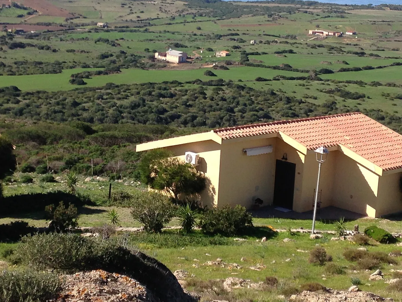 Maison de plain-pied au crépi jaune et toit de tuiles, unité extérieure sur la façade, garrigue rocailleuse et campagne vallonnée