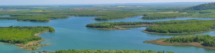 Vue aérienne du lac de Madine, ses îles boisées et la plaine agricole de la Woëvre à l'horizon, dans la Meuse