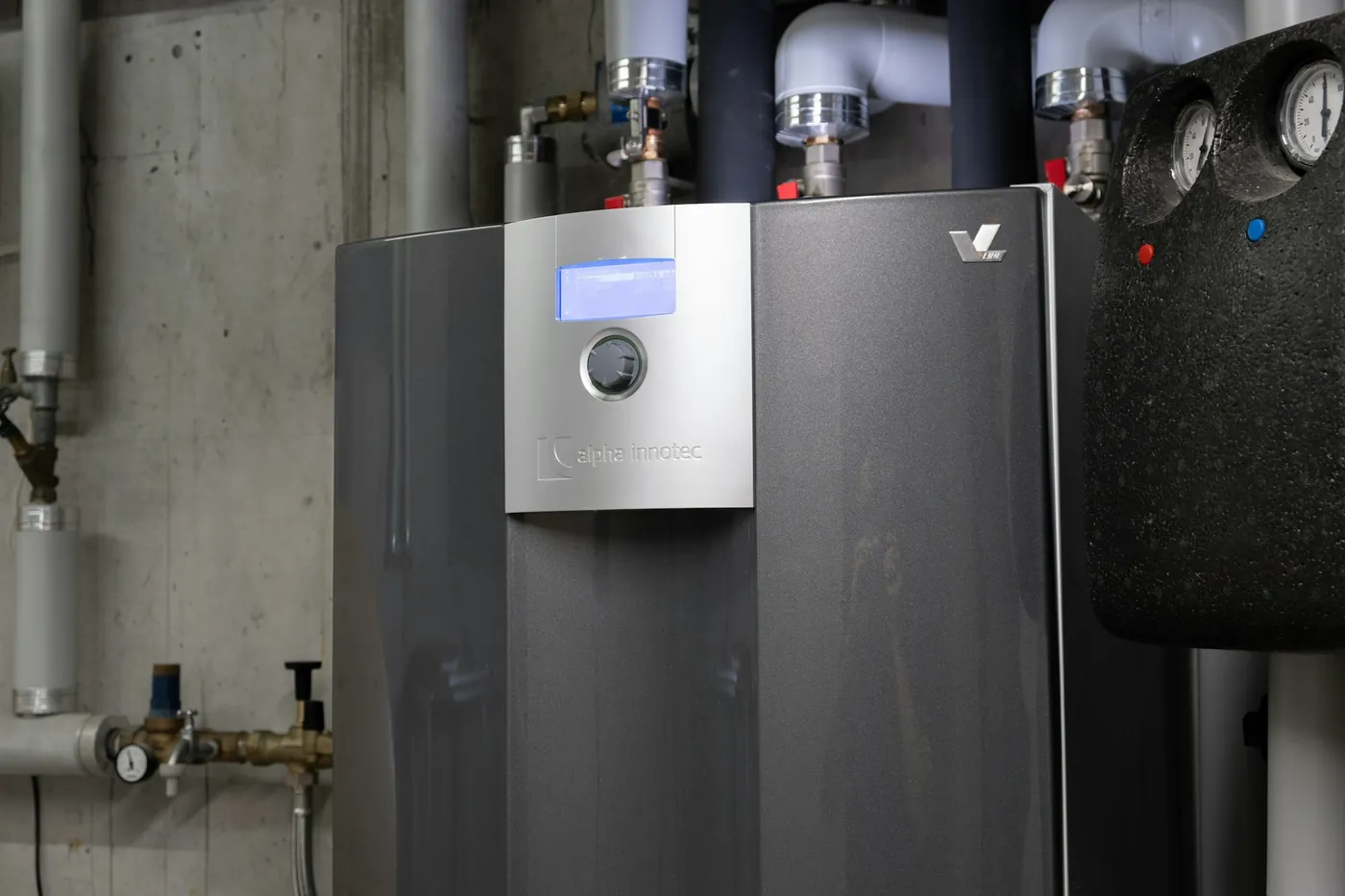 Module intérieur d'une pompe à chaleur air-eau avec écran de réglage et raccordements isolés dans une chaufferie