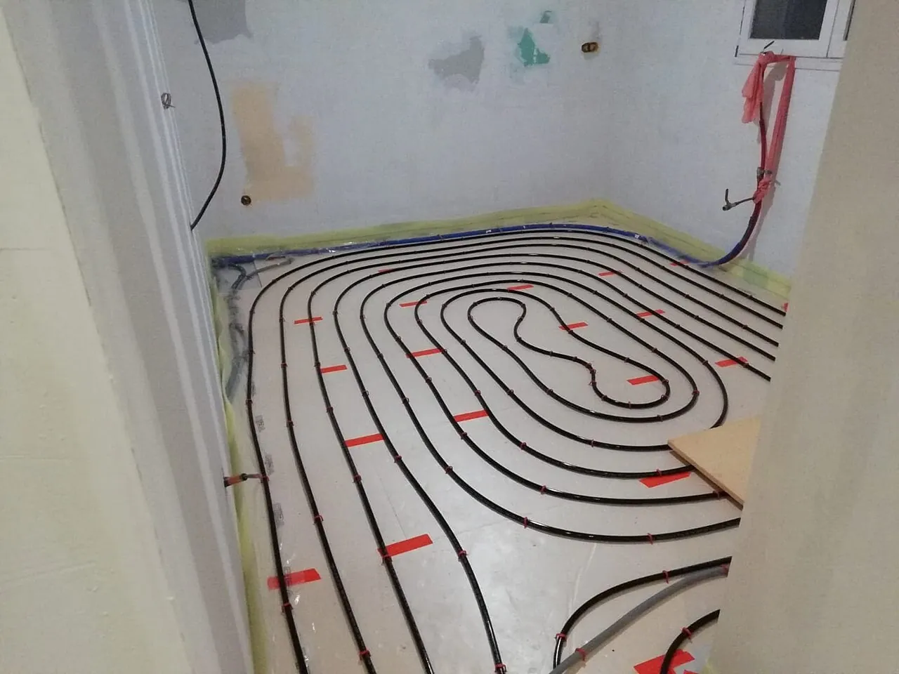 Tubes noirs de plancher chauffant posés en double spirale sur l'isolant d'une petite pièce en travaux, avant la chape