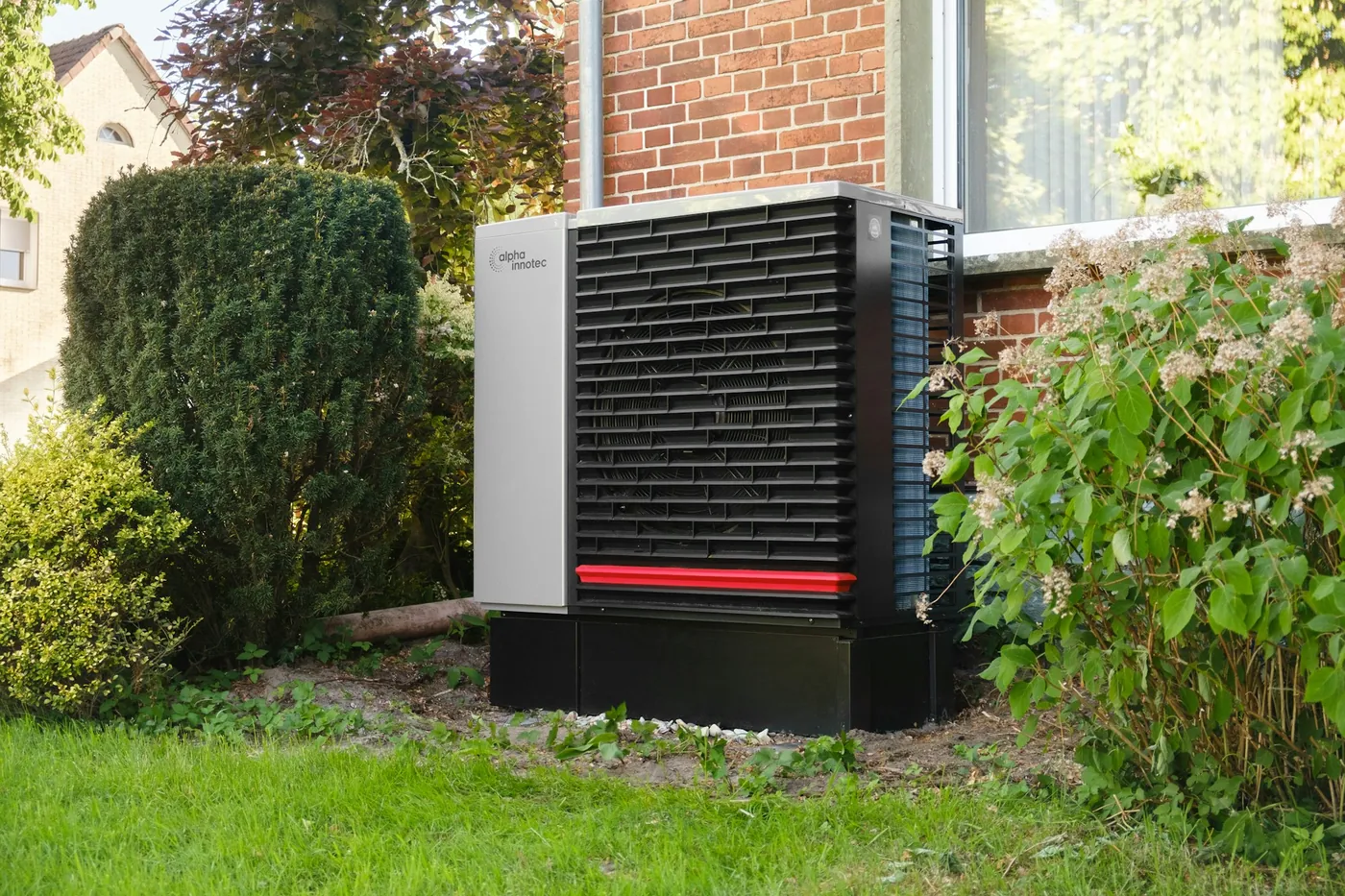 Pompe à chaleur air-eau installée dans le jardin contre une maison en brique, comme on en trouve dans l'agglomération de Troyes