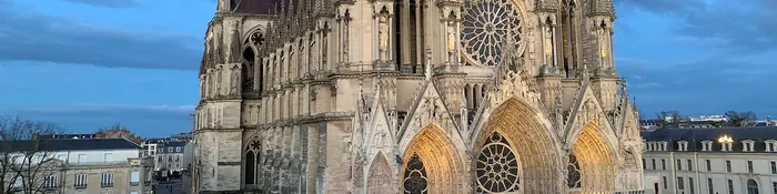 Façade occidentale de la cathédrale Notre-Dame de Reims avec sa grande rose et ses portails éclairés, au crépuscule
