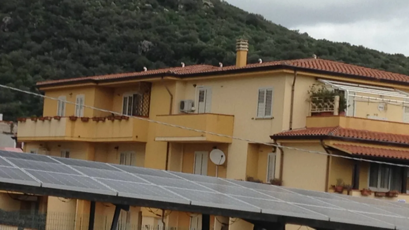 Résidence ocre à toits de tuiles adossée à une colline de maquis, unité extérieure près d'une fenêtre, ombrière photovoltaïque devant