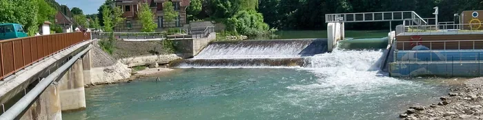 Déversoir de Saint-Julien-les-Villas sur la Seine en été, avec le pont, la chute d'eau et une maison en brique sur la berge
