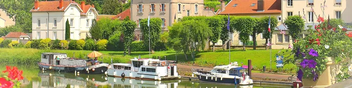 Quais de la Meuse à Saint-Mihiel avec bateaux de plaisance amarrés, maisons aux toits orange et côte boisée