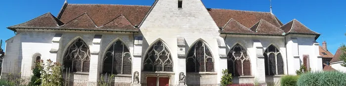 Église de Sainte-Savine en pierre blanche avec ses baies flamboyantes et son jardin de plantes, sous un ciel bleu