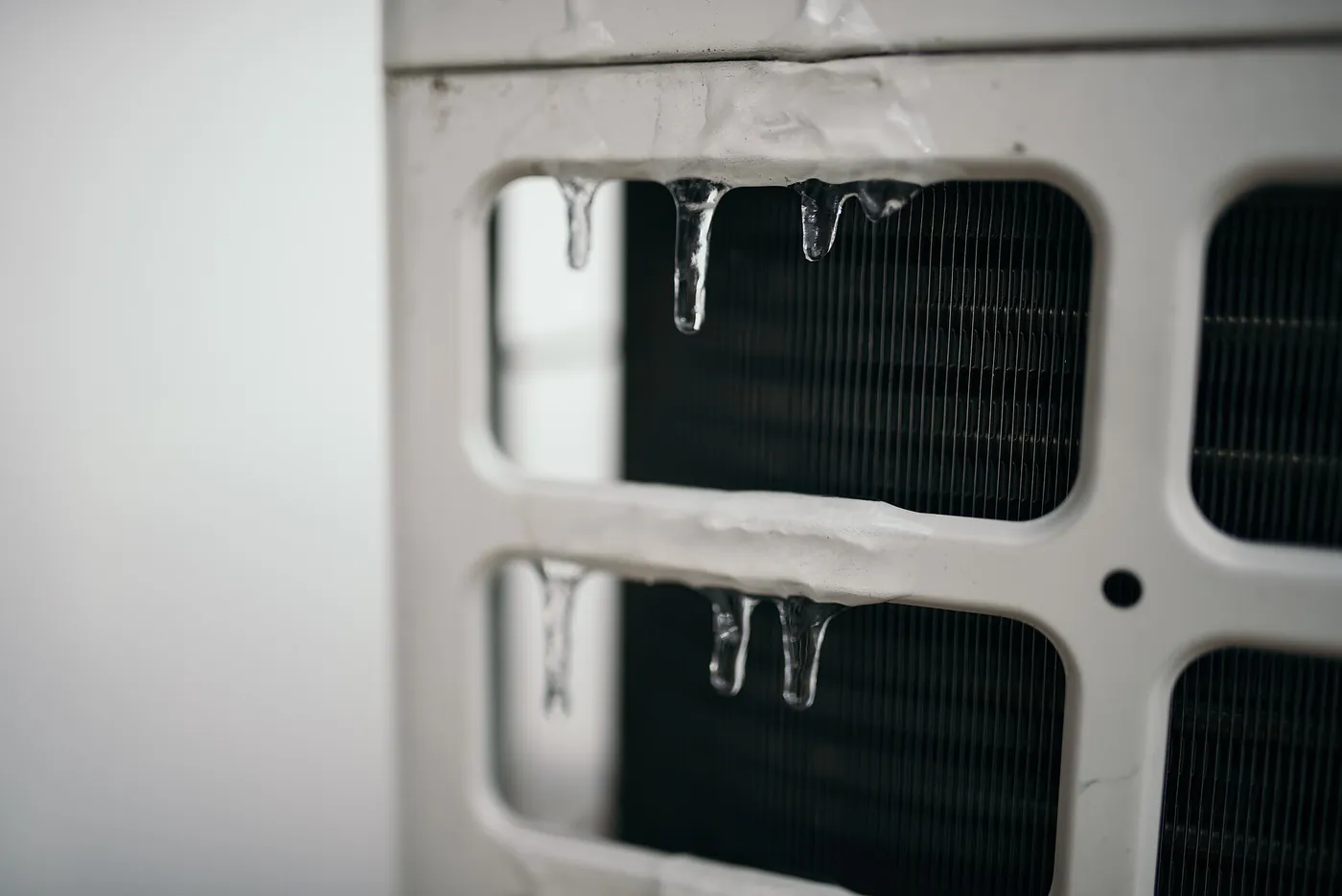 Gros plan sur des stalactites de glace accrochées à la grille d'une unité extérieure de pompe à chaleur, échangeur à l'arrière