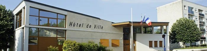 Hôtel de ville contemporain de Tinqueux, façade claire et vitrée avec drapeaux, à côté d'un petit immeuble résidentiel
