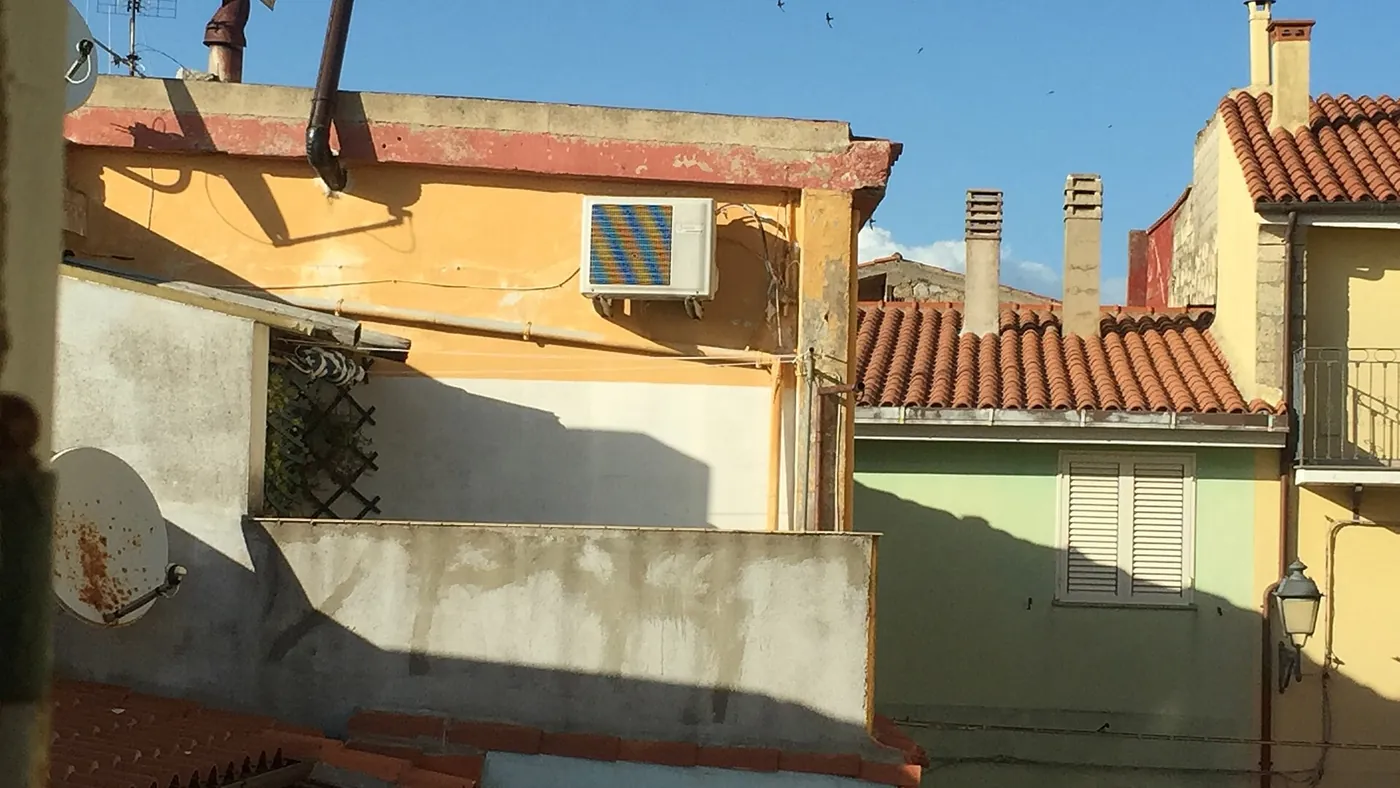Toits de tuiles rondes et façades ocre et vert pâle, unité extérieure en haut d'un mur sous un parapet rouge, comme on en voit à Martigues
