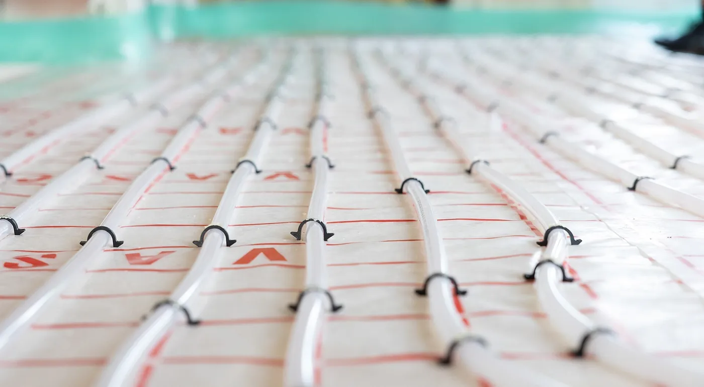 Vue rasante sur des rangées de tubes blancs de plancher chauffant clipsés sur un isolant marqué de repères rouges