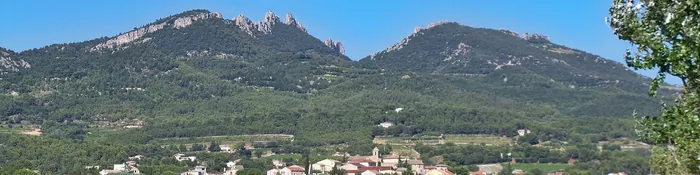 Vignes au premier plan, village de Vacqueyras et crêtes calcaires des Dentelles de Montmirail sous un ciel bleu, dans le Vaucluse